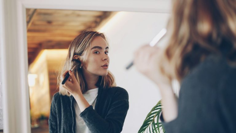 Inicio 17 Young woman applying makeup in mirror